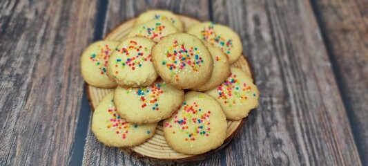 Homemade Rainbow sprinkled butter cookies served in wooden tray on wooden table.