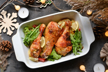Winter festive food concept. Top view of dark vintage background, garland and candles. Christmas and New Year background. Baked chicken legs and potatoes.