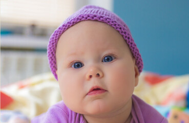 Little baby girl posing in purple bodysuit and knitted hat lying on the bed