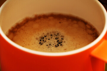 Coffee in a bright orange сup on the table. Close-up is a light green coffee maker with an orange cup.