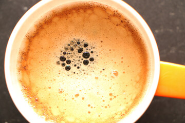 Coffee in a bright orange сup on the table. Close-up is a light green coffee maker with an orange cup.