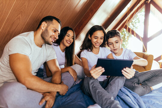 Latin Family Together In Bed In The Morning. Sister And Brother Using Digital Tablet