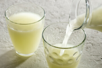 Pouring natural whey from a jug into a glass on a bright background