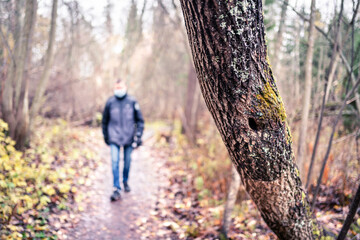 Corona depression, anxiety, loneliness and social distancing concept. Lonely sad man walking in forest alone during coronavirus isolation wearing a mask. Mental health issues and stress from virus.