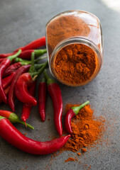 Red chili peppers and paprika powder in glass spice jar on stone table. Dark grey background with copy space. Ingredients top view photo. Vegetable texture close up. 
