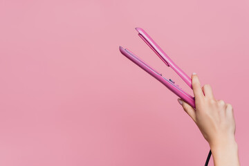 partial view of woman holding hair straightener in hand isolated on pink