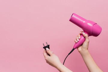 cropped view of woman holding cable with plug and hair dryer isolated on pink