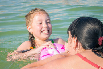 Mom and daughter are having fun at sea. A woman teaches a child to swim. Active family recreation on the water.