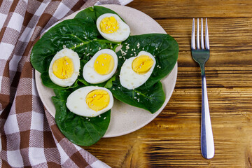 Boiled eggs with fresh spinach leaves and sesame seeds on wooden table. Top view