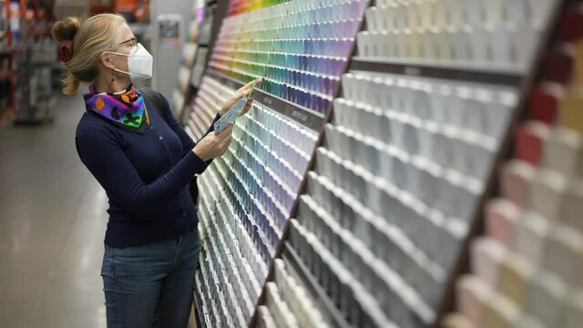 Woman wearing face mask looking at paint chips in a hardware store. Concept of cornonavirus shopping experience.