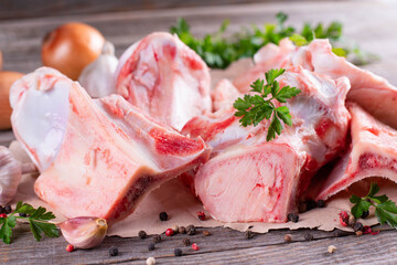 Fresh beef bone on wooden background with vegetables and herbs on the background