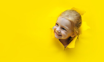 Funny redhead girl peeking through the hole on yellow paper and smiling. The concept of surprise,...