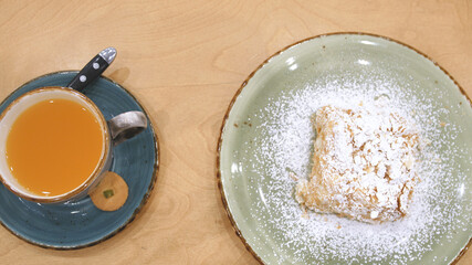 Tasty dessert and sea buckthorn tea. Slice of Napoleon cream cake, made from puff pastry, lies on a plate on a table in a restaurant or cafe.