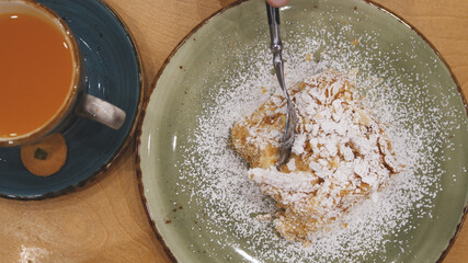 Tasty dessert and sea buckthorn tea. Slice of Napoleon cream cake, made from puff pastry, lies on a plate on a table in a restaurant or cafe.