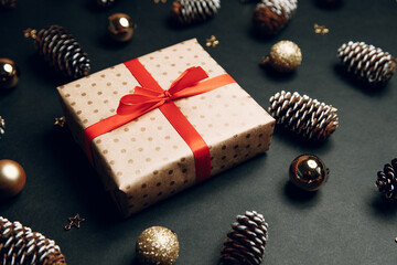 Christmas composition with a gift in a box. Golden toys, modern holiday decorations, gift boxes, fir branches on a dark black background. Elegant Christmas greeting card template.