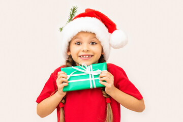 Beautiful little girl posing in a red t-shirt and Christmas hat holding a gift.