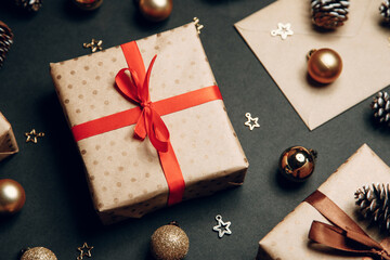 Christmas composition with a gift in a box. Golden toys, modern holiday decorations, gift boxes, fir branches on a dark black background. Elegant Christmas greeting card template.