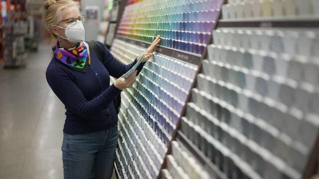 Woman wearing face mask looking at paint chips in a hardware store. Concept of cornonavirus shopping experience.
