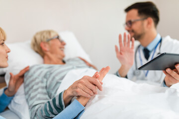 Fototapeta premium Young doctor visiting sick senior woman with her daughter in hospital room or nursing center.