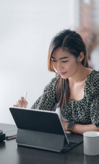 Portrait of young beautiful asian woman working on tablet computer while sitting at home.