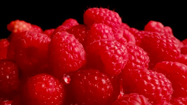 Colorful pile of red raspberries rotating on isolated black background, Closeup