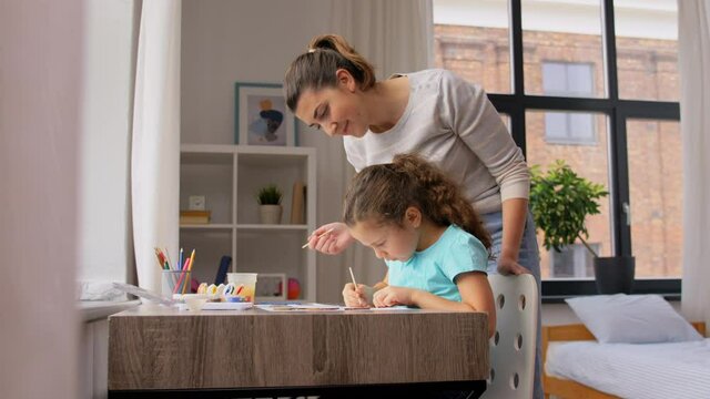 family, motherhood and leisure concept - mother spending time with her little daughter drawing with colors at home