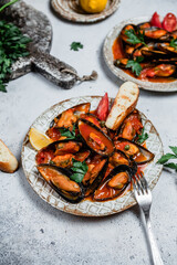mussels in tomato sauce with fresh herbs and toasted baguette on grey background, top view, comfort food concept