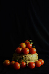 Fototapeta na wymiar Rustic bowl with cherrys tomatoes and more scattered on black cloth, light entering from the side