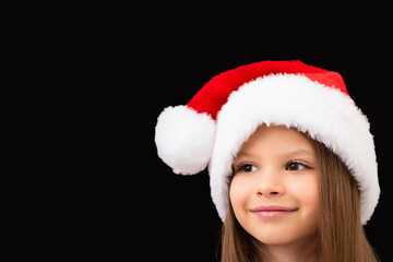 A cute little girl in a Christmas hat is smiling.