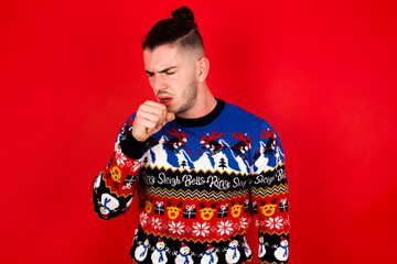 Young handsome Caucasian man wearing Christmas sweater against red wall, feeling unwell and coughing as symptom for cold or bronchitis. Healthcare concept.