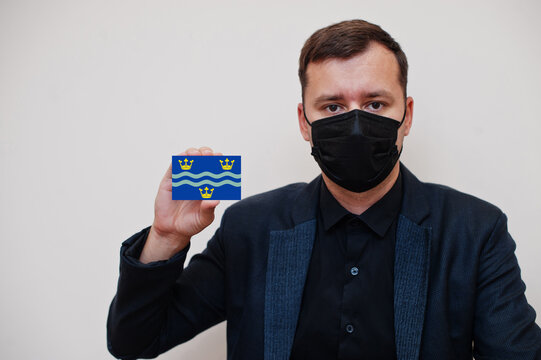 Man wear black formal and protect face mask, hold Cambridgeshire flag card isolated on white background. United Kingdom counties of England coronavirus Covid concept.