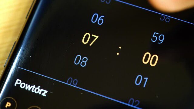 Setting an alarm clock on a modern smartphone, 7:00, 7 AM, detail, closeup, Finger touching the mobile phone device display, alarm app set up, macro shot. Waking up early morning abstract concept