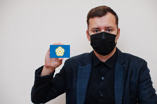 Man wear black formal and protect face mask, hold Yorkshire flag card isolated on white background. United Kingdom counties of England coronavirus Covid concept.