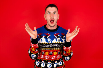 Surprised terrified Young handsome Caucasian man wearing Christmas sweater Gestures with uncertainty, stares at camera, puzzled as doesn't know answer on tricky question, People, body language.