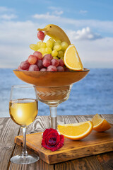 A banana in the shape of a dolphin, grapes and a glass of white wine with oranges on the background of the sea.