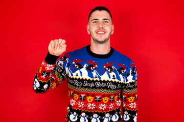 Young handsome Caucasian man wearing Christmas sweater against red wall,  pointing up with fingers number ten in Chinese sign language Shi