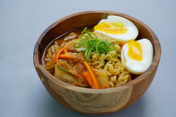 Ramyeon (Korean instant noodles soup) on wooden bowl and chopsticks in blue stripes napkin in isolated gray background 