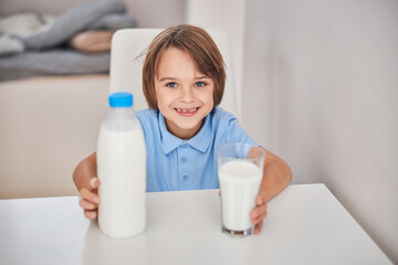 Fototapeta na wymiar Cheerful little boy smiling and holding glass of milk