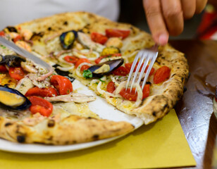 Eating of Italian pizza with sea food, small red tomatoes and fresh basil