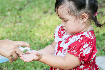 A cute Asian girl wearing a red vintage dress is washing her hands with alcohol gel after playing in the playground.