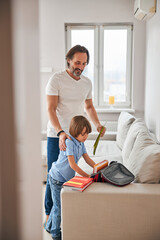 Happy father assisting his kid with packing a school-bag