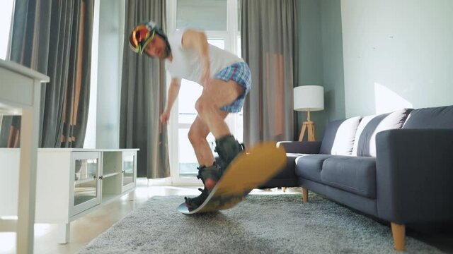 Fun video. Man in shorts and a T-shirt depicts snowboarding on a carpet in a cozy room. Waiting for a snowy winter