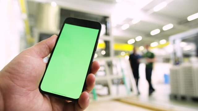 Smartphone in Industrial plant with green screen. Greenscreen smart phone holding in bright industry building with engineers in background. Iot app 