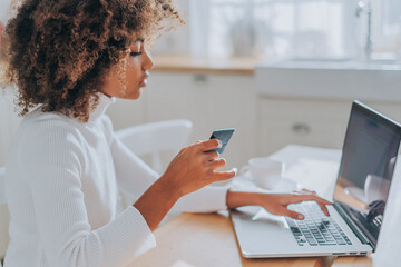 Lady with perfect dark skin holding credit card and inserting bank information for online shopping...