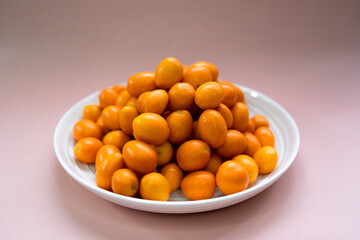 kumquats in white plate on a pale pink background