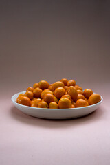 kumquats in white plate on a pale pink background