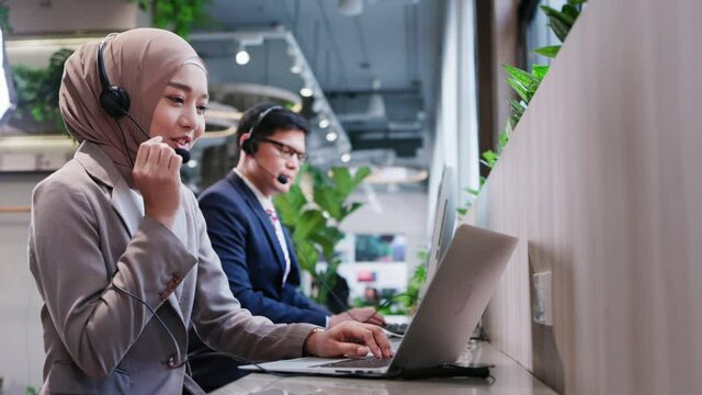 Muslim woman work as a Call Center In a modern office by social distancing with colleagues. Information service, consultation or video conference. Concept key worker