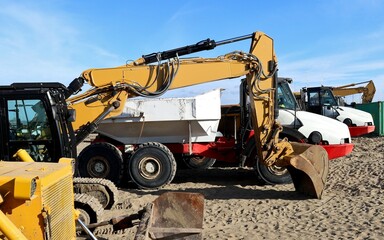 Yellow excavators and white dumping trucks lined up on the sand.