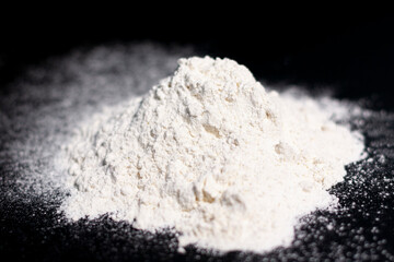 Fototapeta na wymiar A mound of white flour on a dark surface. Top view.