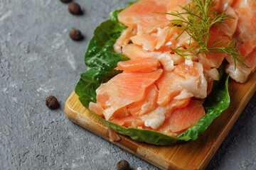 Pieces of fried salmon with dill and lemon wedges on a wooden board